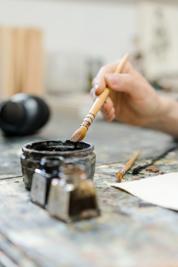 Demonstrating the use of different types of paintbrushes, with a large brush being dipped into black paint.