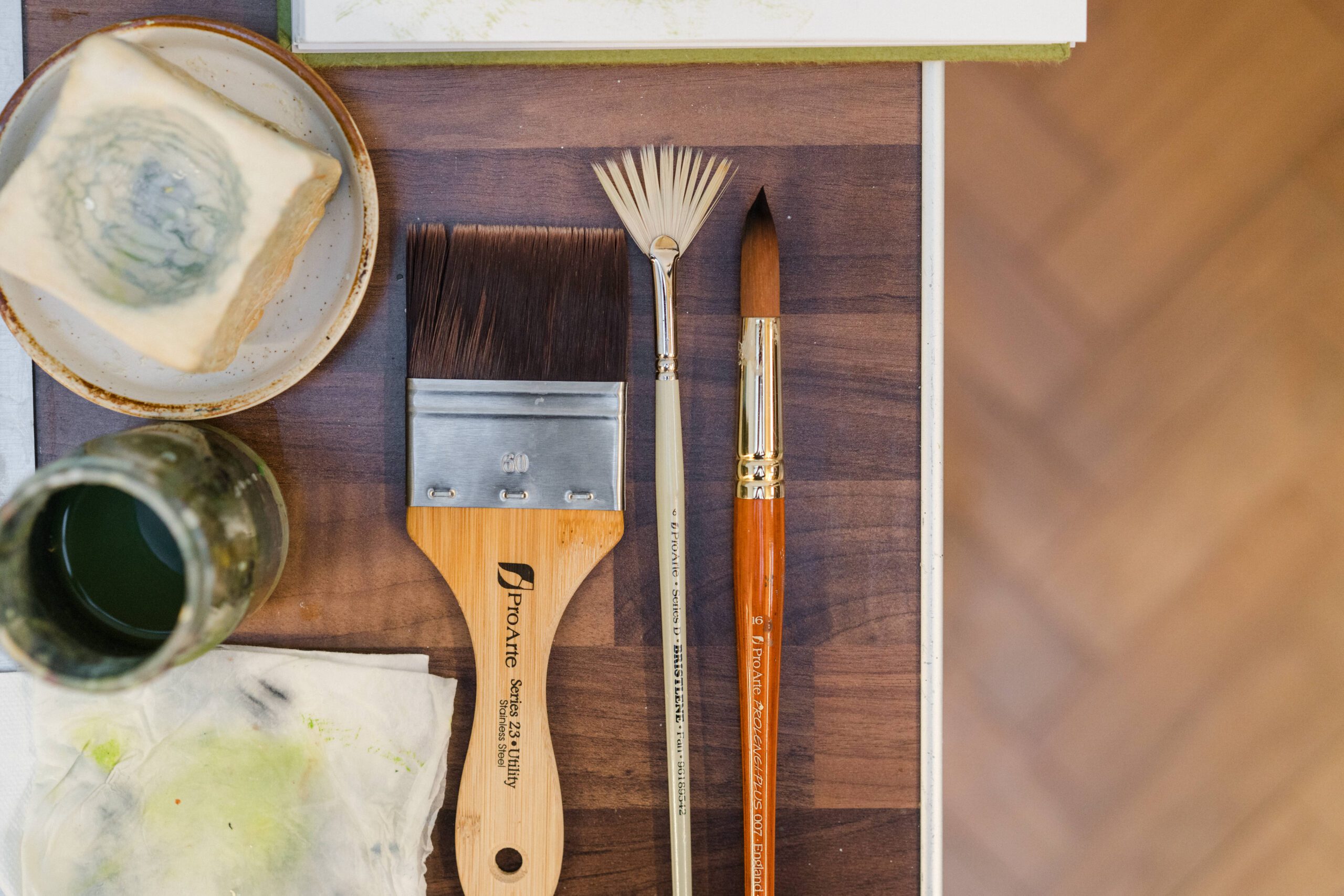 various paintbrushes on a wooden table alongside painting equipment