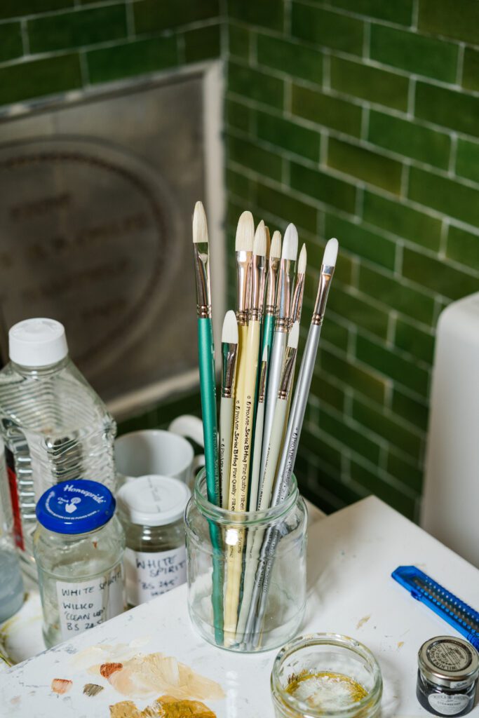 Different types of paintbrushes in a glass jar in an artist studio.