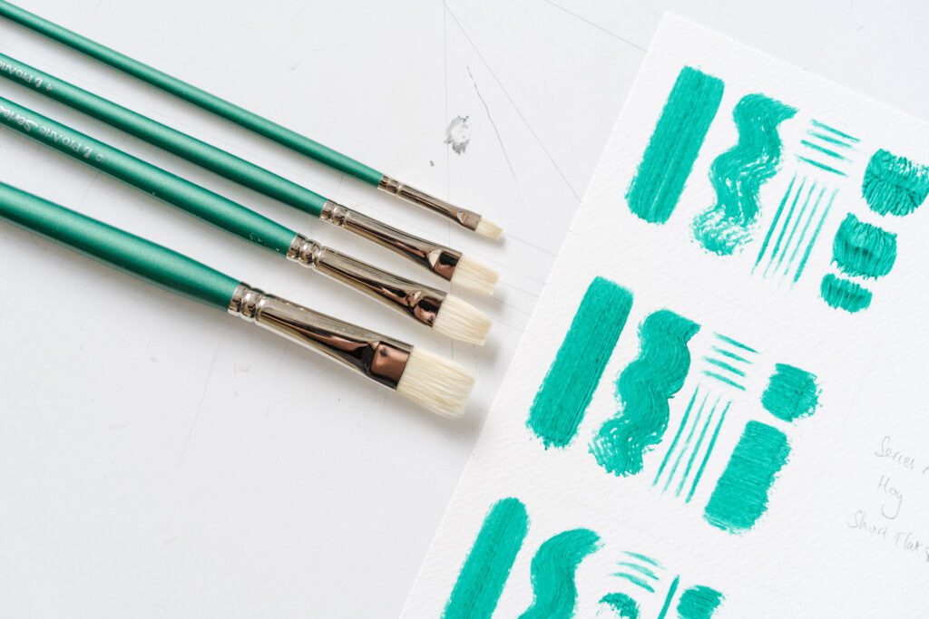 various sized paintbrushes alongside green brushstrokes on paper