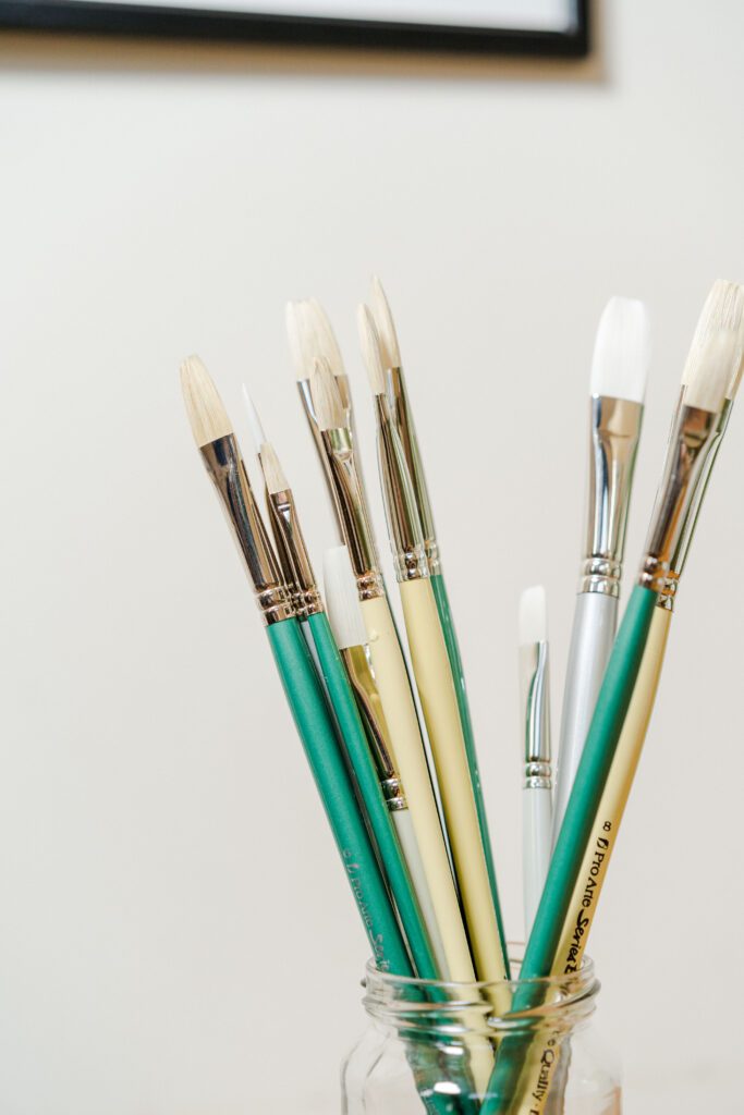 Different types of paintbrushes in a glass jar, against a white background.