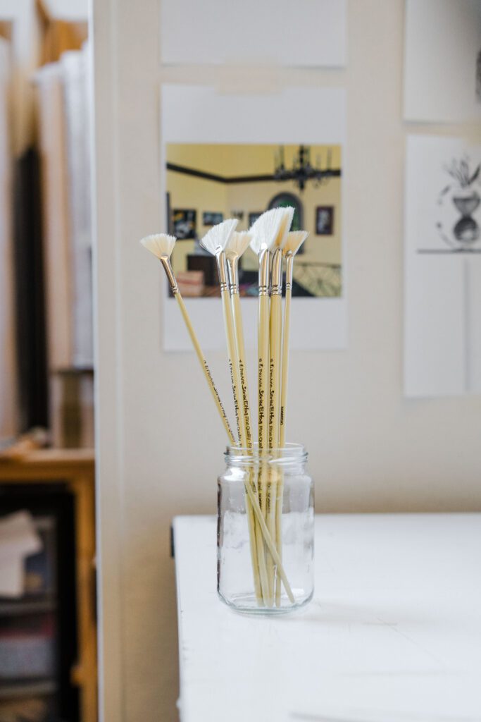 Different types of paintbrushes in a glass jar in an artists studio.