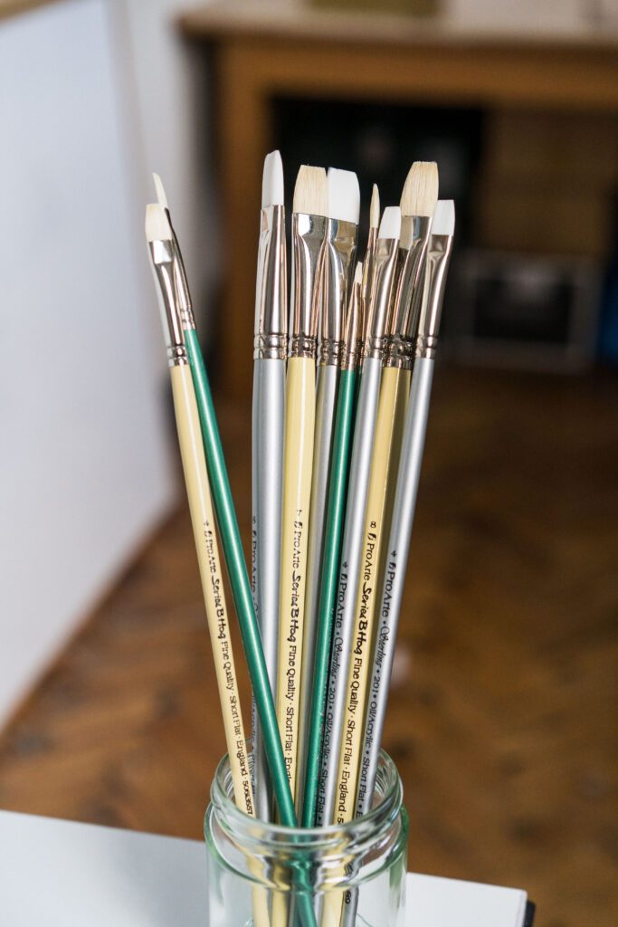 Different types of paintbrushes in a glass jar in a studio setting.