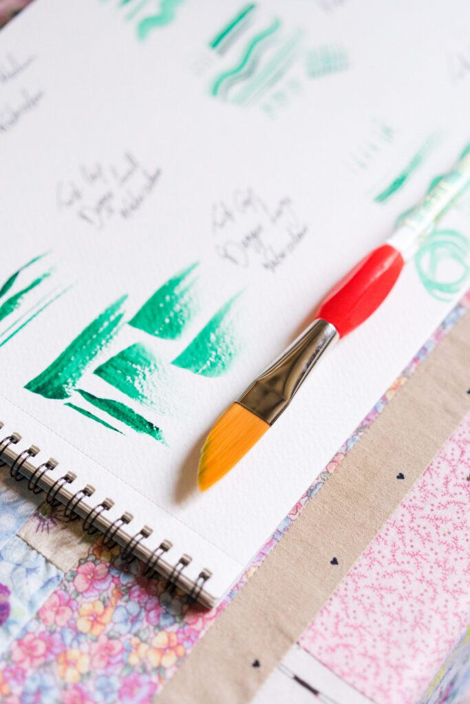 Different types of dagger paintbrushes next to various brushstrokes in green paint on white paper.