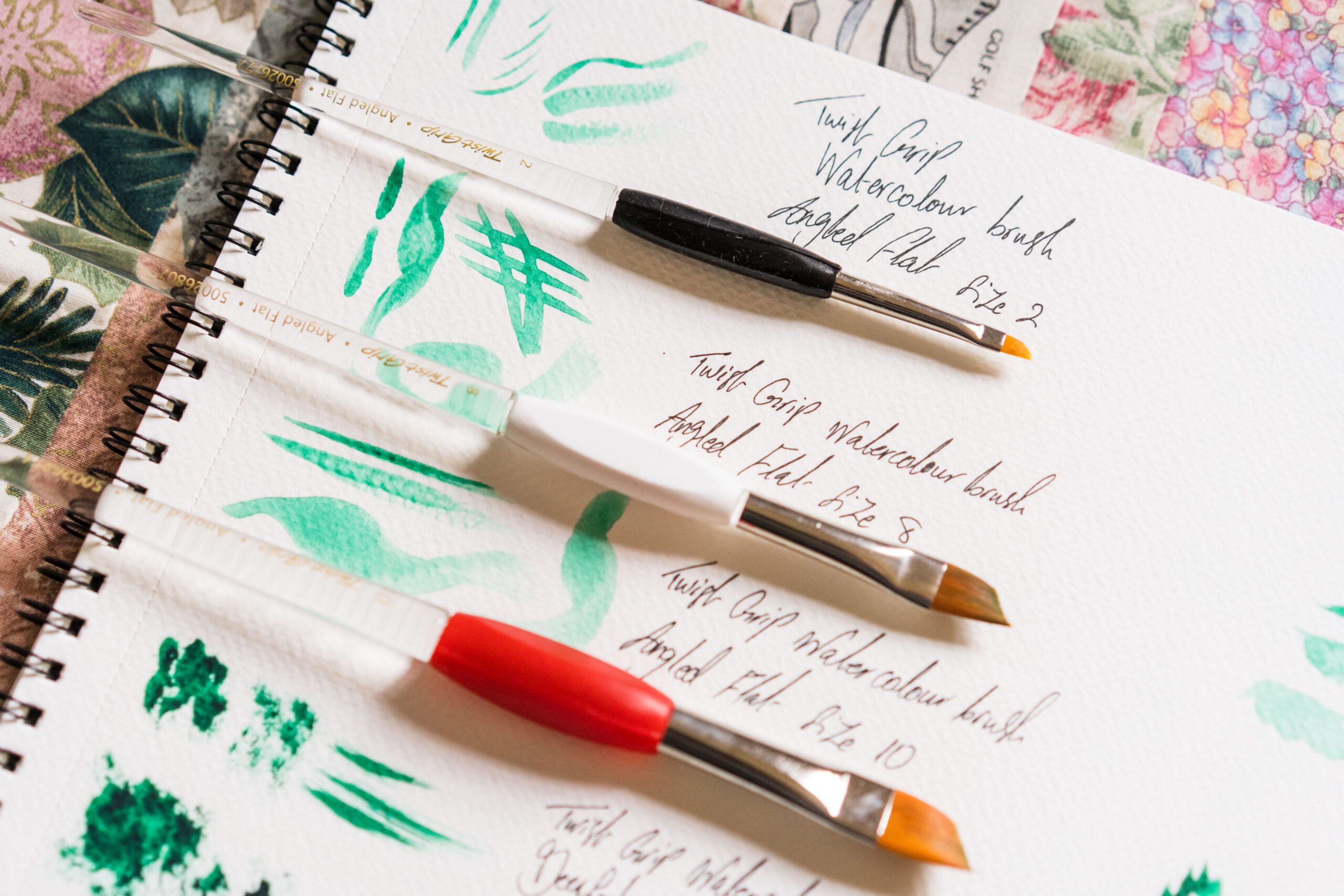 various sized paintbrushes on top of a sketchbook