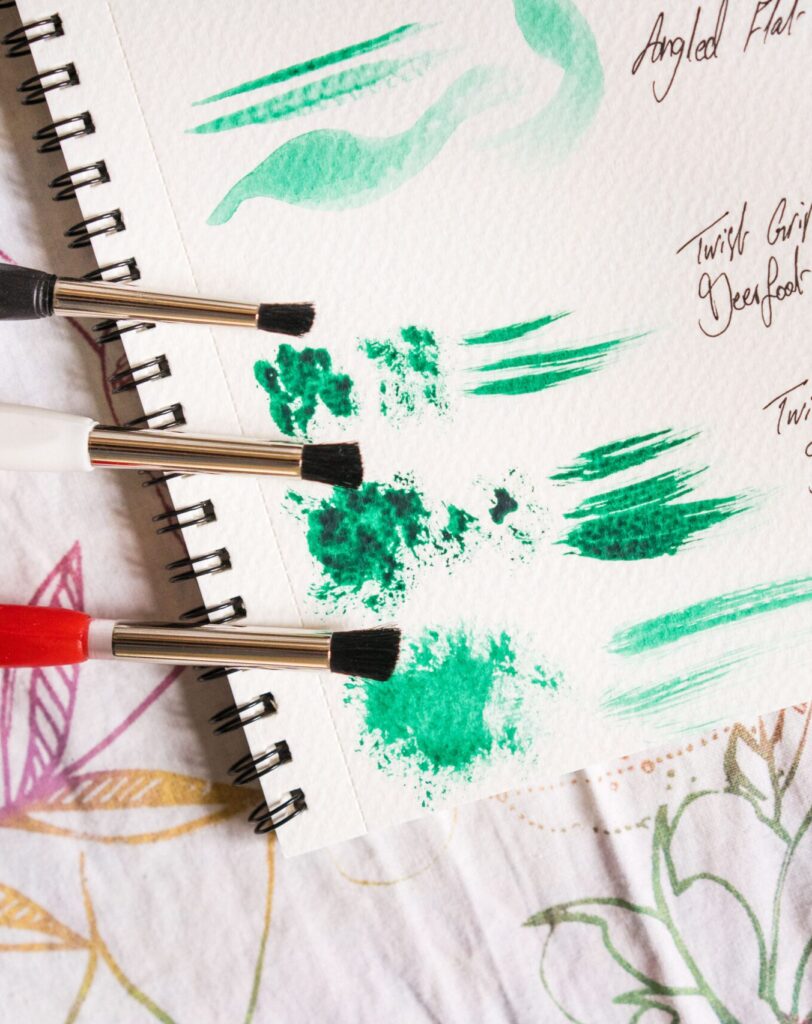 Two different types of paintbrushes next to various brushstrokes in green paint on white paper.
