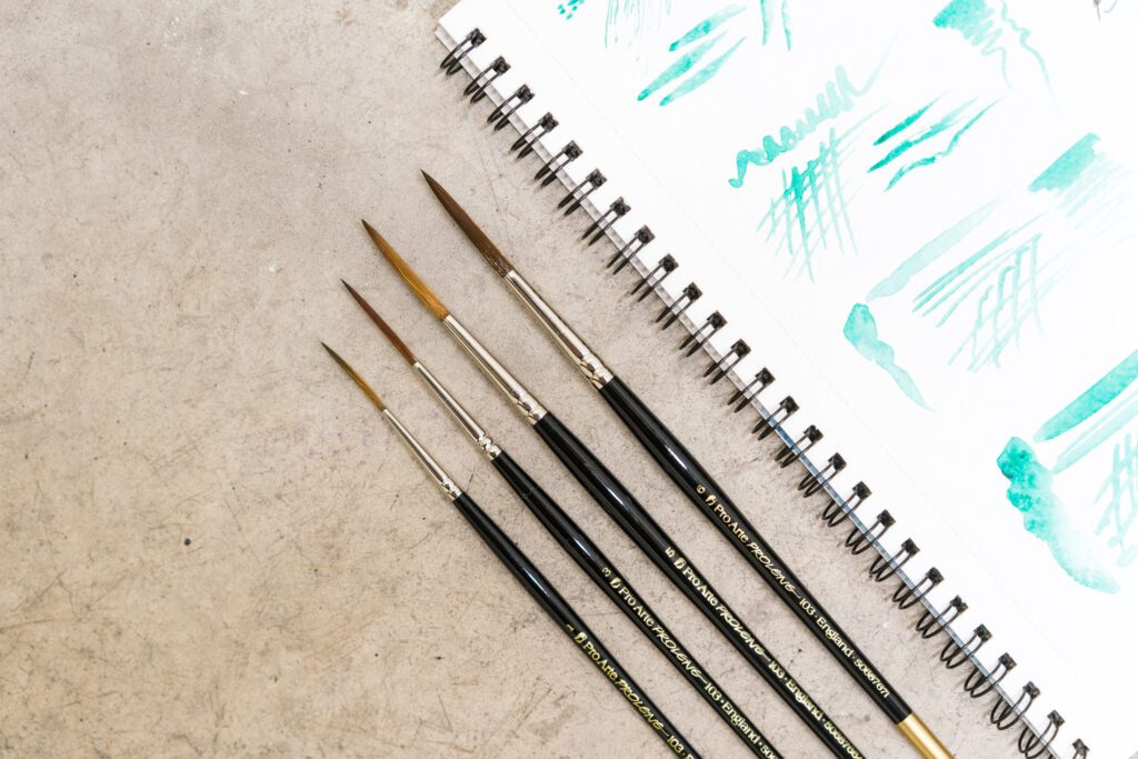 Various size paintbrushes alongside a sketchbook