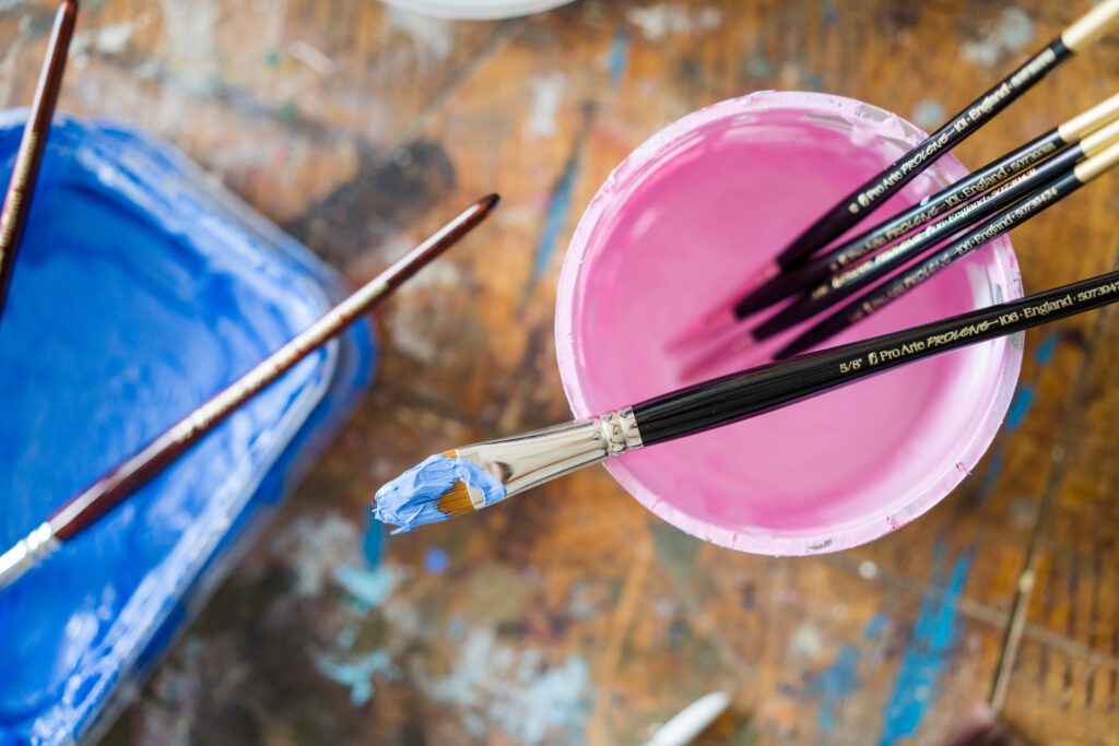 Image shows paintbrushes in a pot of water alongside a dish of blue paint
