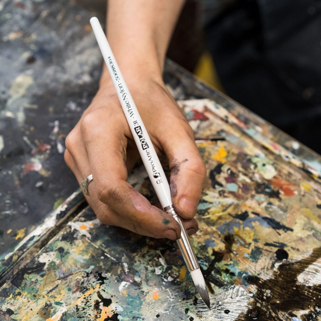 Close up of an artist holding a paintbrush to add brushstrokes to an abstract artwork with many colours