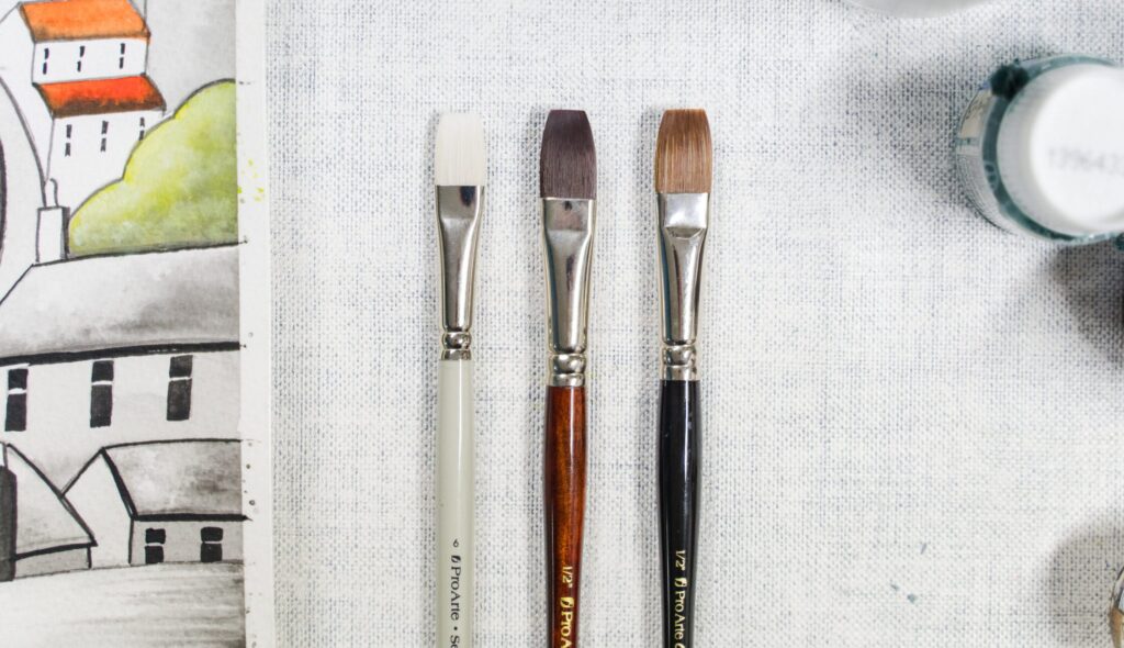 three paintbrushes side by side, one with a white handle, one with a red handle, one with a blue handle