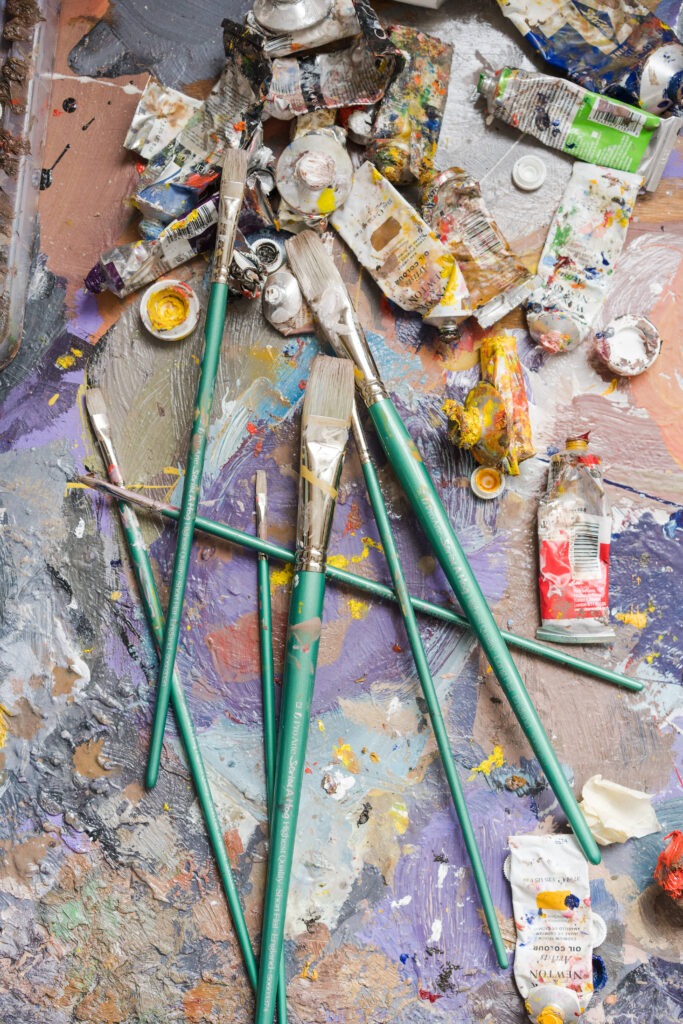 A close-up of a well-used oil paint tubes, showcasing the vibrant colors and messy charm of an artist's tools, alongside used Pro-Arte paintbrushes.