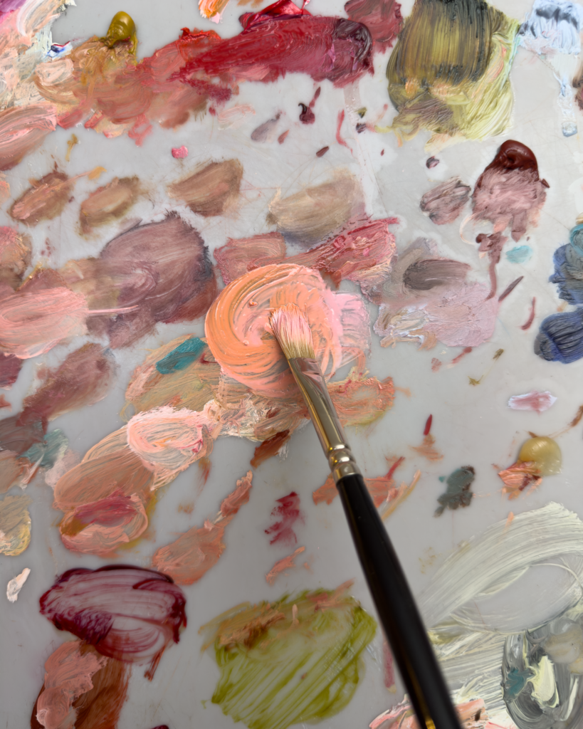 Brush picking up peach coloured oil paint from a palette.