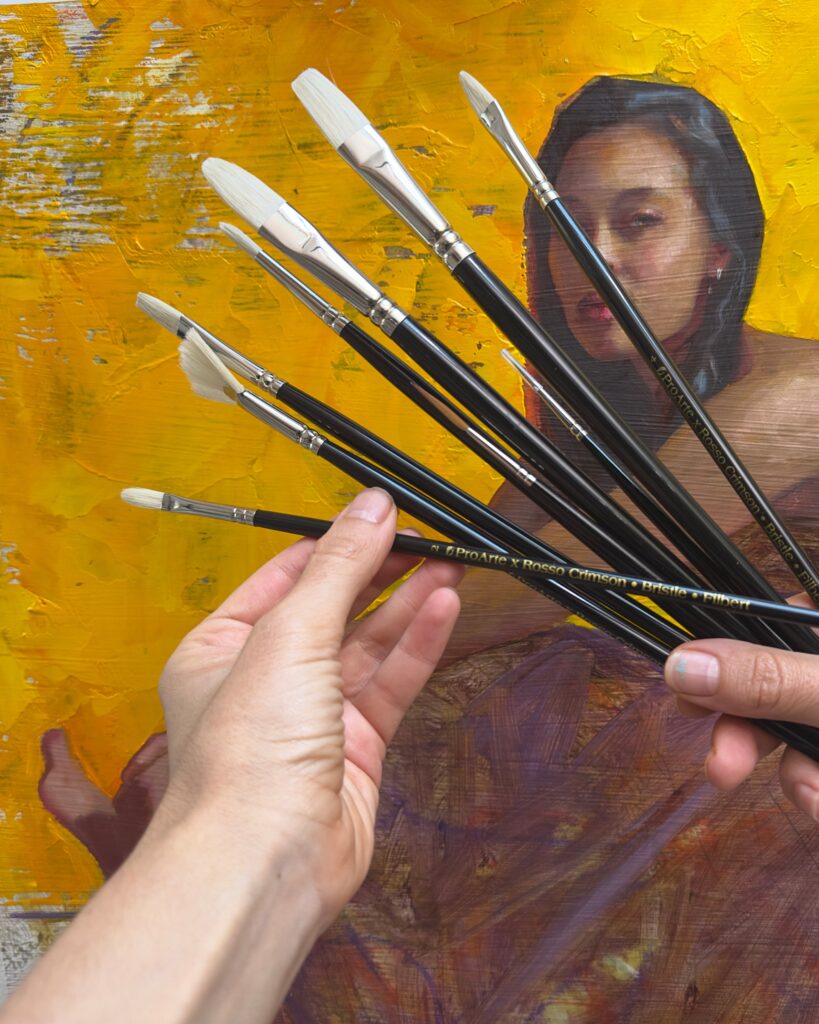 Rosso Crimson x Pro Arte Hog Hair Brushes held above a Rosso Crimson oil painting.